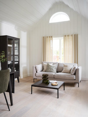 Ljust vardagsrum med beige soffa, svart soffbord, vitlaserade väggar och halvmåneformat fönster