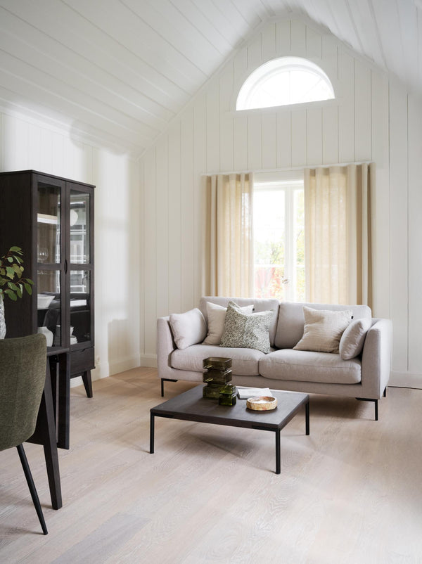Ljust vardagsrum med beige soffa, svart soffbord, vitlaserade väggar och halvmåneformat fönster