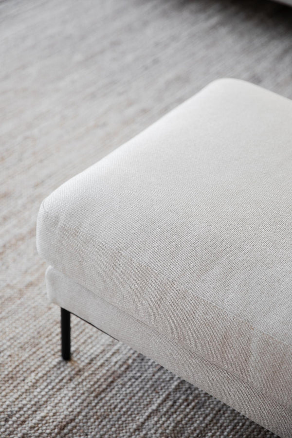 Vit stoppad pall med linneklädsel och svarta ben på en ljusgrå matta i skandinavisk stil