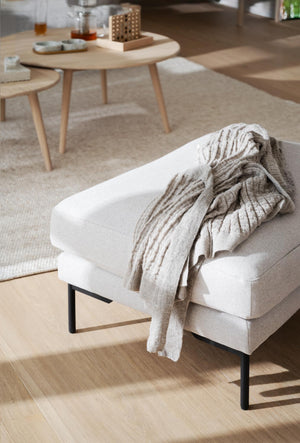 Vit stoppad sittpuff med svarta ben och beige pläd i skandinavisk vardagsrumsmiljö med träbord