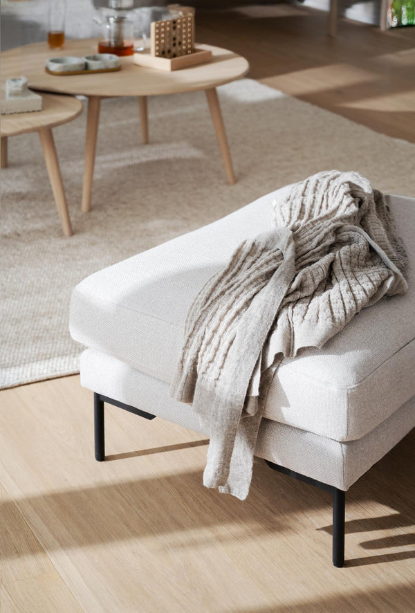 Vit stoppad sittpuff med svarta ben och beige pläd i skandinavisk vardagsrumsmiljö med träbord