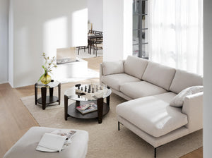 Beige hörnsoffa med schäslong i minimalistiskt vardagsrum med runda soffbord och ljust trägolv