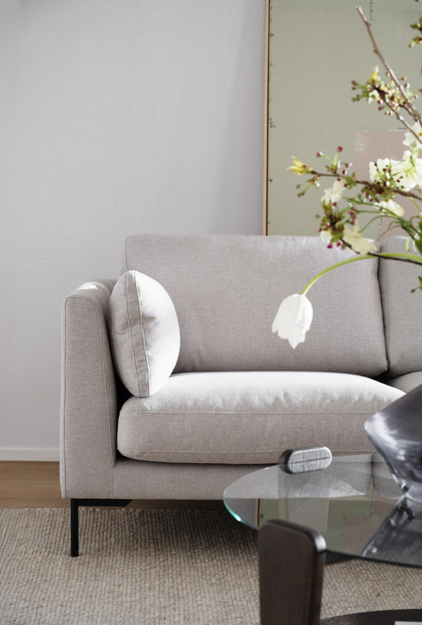 Grå tvåsitssoffa med vita kuddar och tulpan i minimalistiskt vardagsrum med spegel