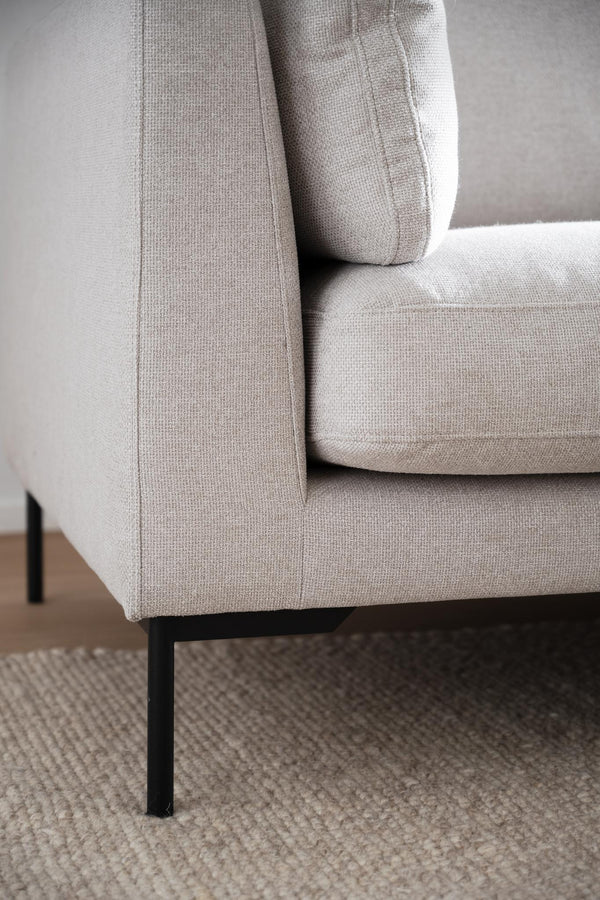 Beige soffa med svarta metallben på beige matta, närbild av hörn med dyna