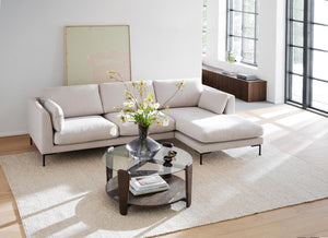 Ljusgrå soffgrupp med schäslong och runt soffbord i vardagsrum med stora fönster och naturligt ljus