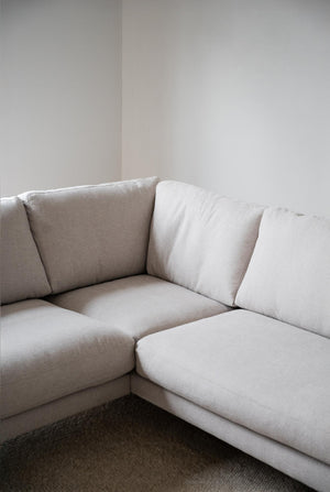 Ljusgrå hörnsoffa med lösadynor i minimalistisk vardagsrumsmiljö med mörk matta