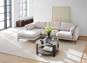 Beige schäslong-soffa med svarta ben i ljust vardagsrum med runt soffbord och stora fönster