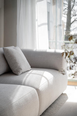 Ljusgrå soffa med kudde vid fönster med vita gardiner i minimalistiskt vardagsrum