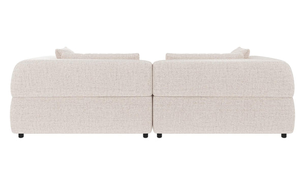 Beige modulsoffa i två delar med kuddar, sedd bakifrån mot vit bakgrund