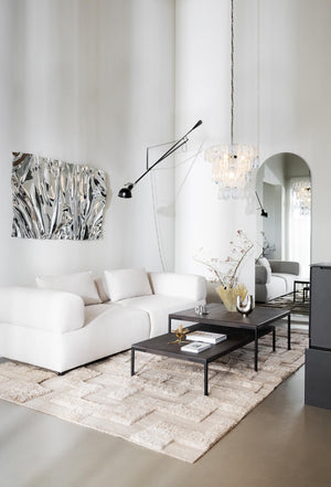 Ljus modern vardagsrum med vit bouclesoffa, svarta soffbord, kristallkrona och beige matta med geometriskt mönster