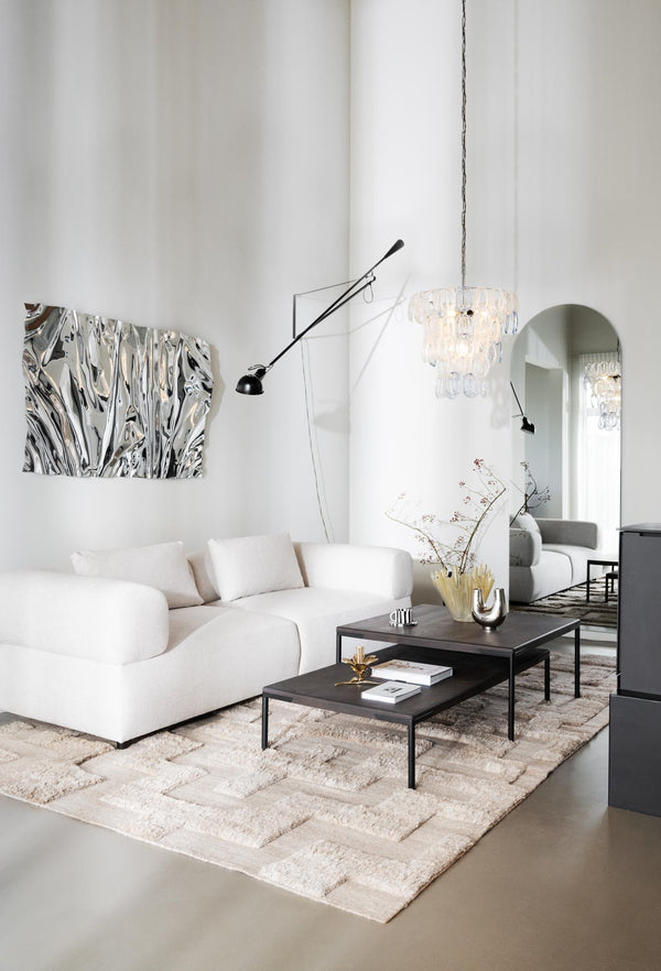 Ljus modern vardagsrum med vit bouclesoffa, svarta soffbord, kristallkrona och beige matta med geometriskt mönster