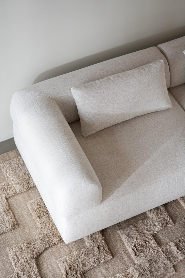 Beige fåtölj med mjuka rundade former och matchande kudde på mönstrad matta