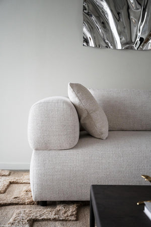 Ljusgrå soffa med rundade armstöd och dynor i modern skandinavisk design mot vit vägg