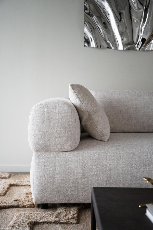 Ljusgrå soffa med rundade armstöd och dynor i modern skandinavisk design mot vit vägg