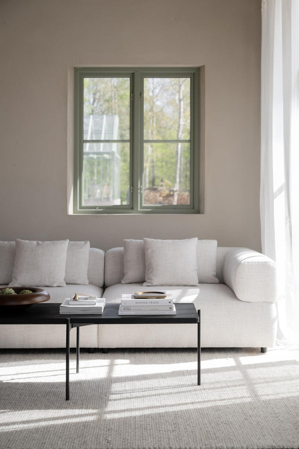 Ljust vardagsrum med beige soffa, svartkoffebord och grönt fönster med utsikt mot natur