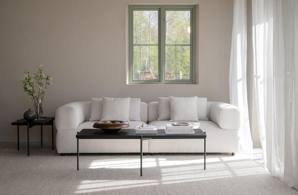 Ljust vardagsrum med beige soffa, svart soffbord och minimalistisk inredning i skandinavisk stil