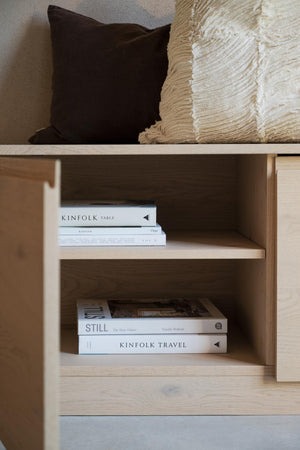 Ljus träbokhylla med Kinfolk-böcker och dekorativa kuddar i svart och beige