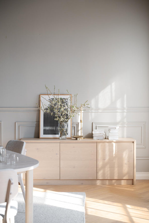 Ljust sideboard i trä med vit väggpanel, vacker dekoration med vas, tavla och ljusstake i skandinavisk stil