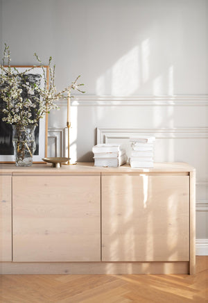 Ljust träskåp med vita böcker och vas med blommor i minimalistisk skandinavisk inredning