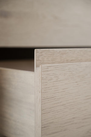 Närbild på hörn av vit låda eller byrå med synlig trästruktur och falsad kant