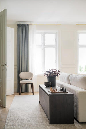 Ljust vardagsrum med beige soffa, svart soffbord, gröna gardiner och minimalistisk inredning i skandinavisk stil