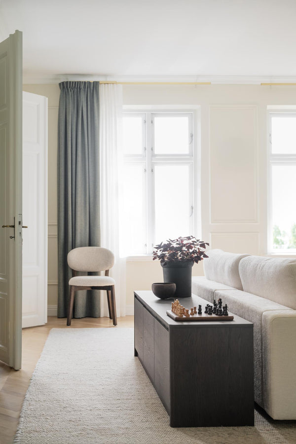 Ljust vardagsrum med beige soffa, svart soffbord, gröna gardiner och minimalistisk inredning i skandinavisk stil