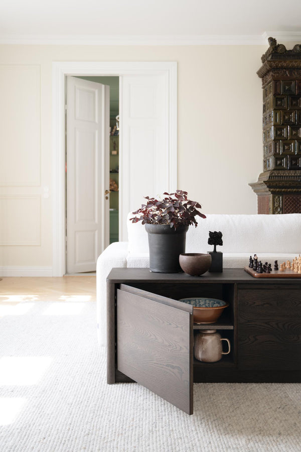 Mörkgrått soffbord med öppen låda som visar förvaring av keramik, dekorerat med växter och schackbräde