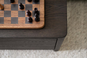Schackbräde i trä med schackpjäser på mörkt soffbord med låda