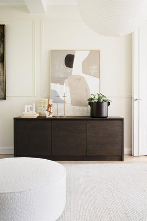 Minimalistiskt sideboard i mörkt trä med abstract tavla, ljusstakar och krukväxt i modern vardagsrumsinredning