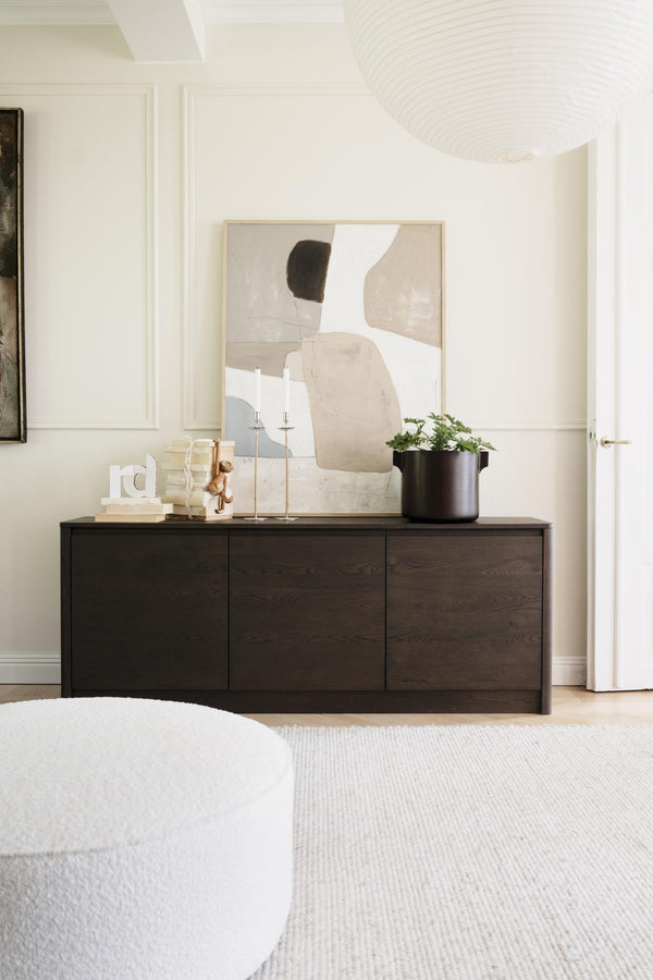 Minimalistiskt sideboard i mörkt trä med abstract tavla, ljusstakar och krukväxt i modern vardagsrumsinredning
