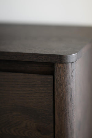 Närbild på möbelhörn i mörkbejsat trä med synlig trästruktur och rundad kant
