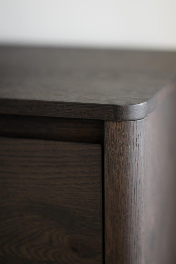 Närbild på möbelhörn i mörkbejsat trä med synlig trästruktur och rundad kant