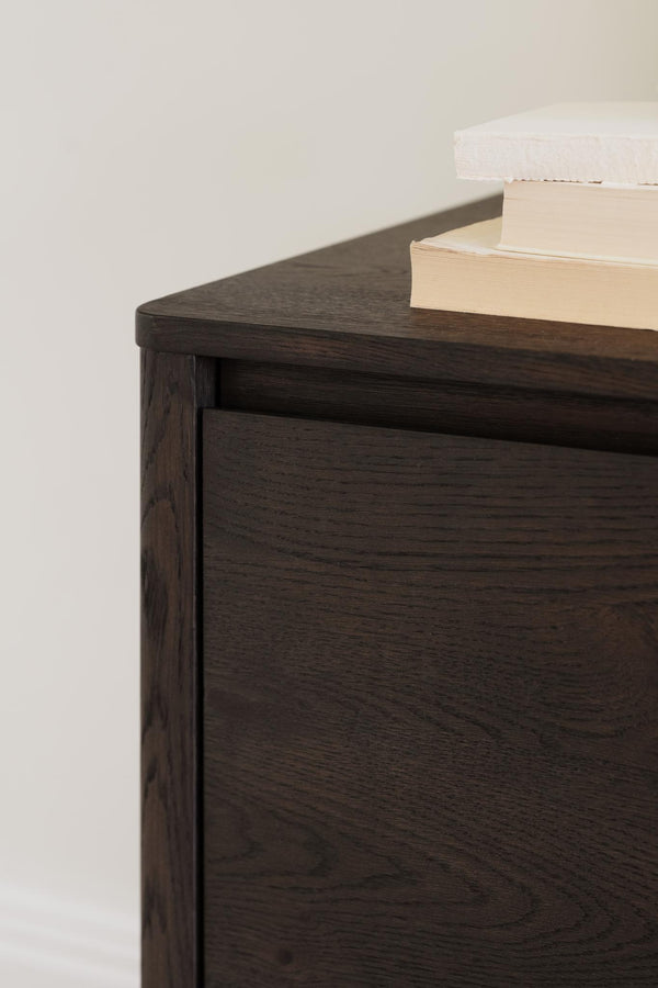 Mörkt sängbord i trä med rundade hörn och böcker på toppen, närbild av modern skandinavisk design