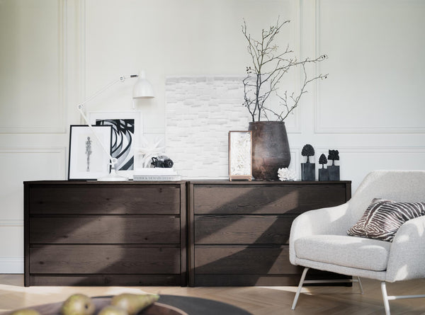 Mörk träkommod med vita väggar, vit fåtölj och dekorativa föremål i skandinavisk stil