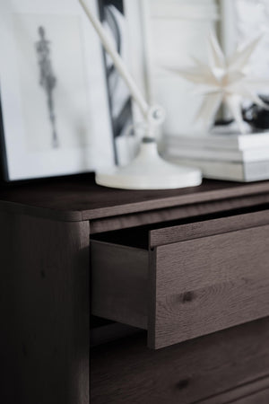 Mörk träbyrå med utdragen låda, dekorerad med vit vas och böcker på toppen