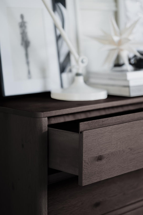 Mörk träbyrå med utdragen låda, dekorerad med vit vas och böcker på toppen