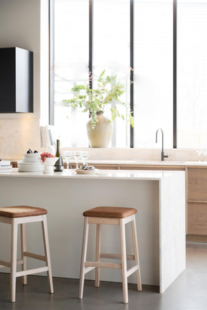 Moderna barstolar i ljust trä vid vitt köksbord med minimalistisk design och naturlig belysning