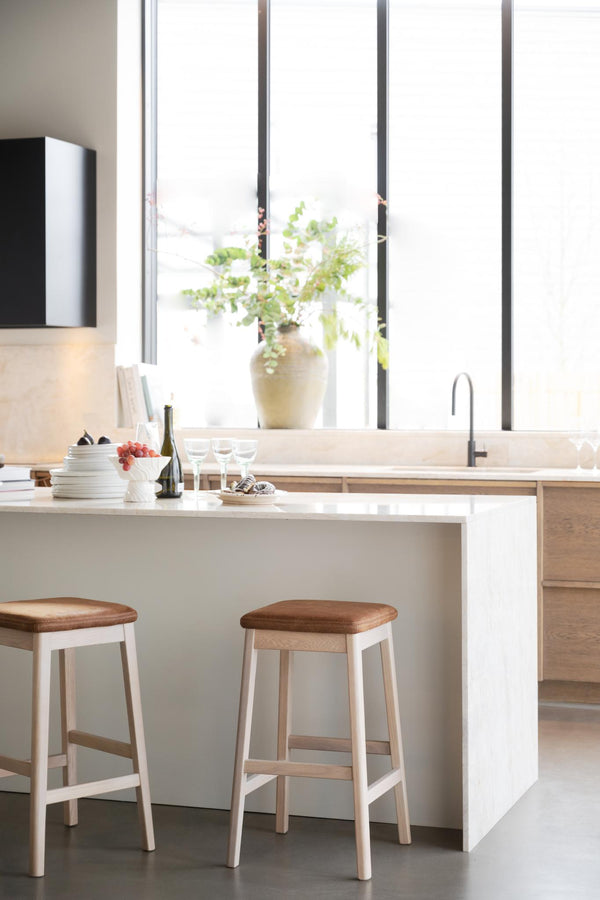 Moderna barstolar i ljust trä vid vitt köksbord med minimalistisk design och naturlig belysning