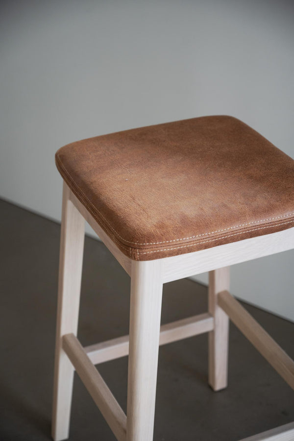 Pall med brunt lädersits och vitlaserade trä ben, kvadratisk sits med synliga sömmar
