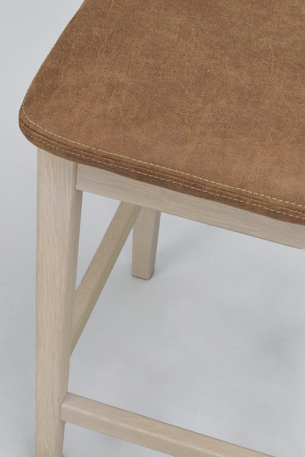 Barstol med brunt läderöverdrag och ljusa träben i vitpigmenterad ek, närbild på sits och ben