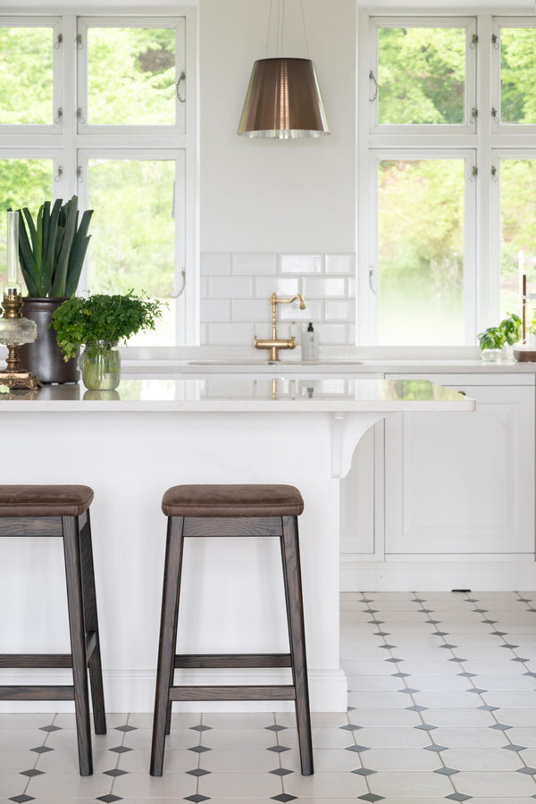 Vitt kök med barstolar, marmorskiva, mässingsblandare och kakelvägg med fönster
