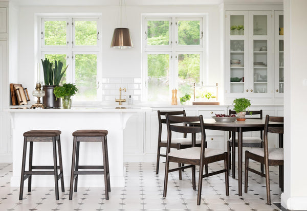 Ljust kök i skandinavisk stil med vita skåp, barstolar i trä, matbord med stolar och glasdörrar