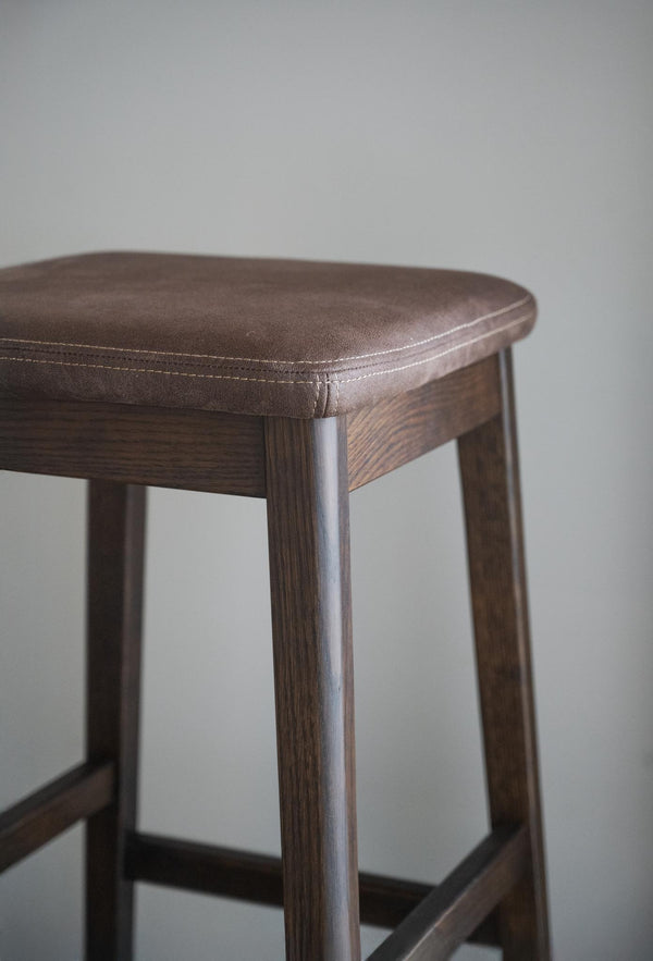 Barpall med brun läderklädd sits och mörkbetsade trästomme i närbild