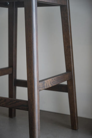 Närbild av möbelben i mörkt trä med synlig trästruktur och horisontella fotpinnar på barstol eller pall