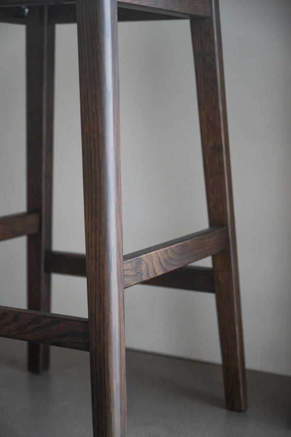 Närbild av möbelben i mörkt trä med synlig trästruktur och horisontella fotpinnar på barstol eller pall