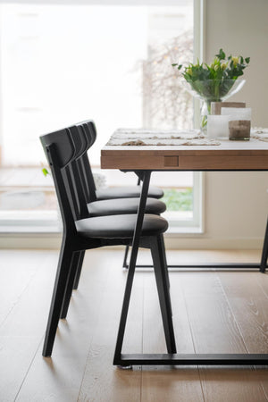 Svart stol med grå dyna vid matbord i trä med blomvas och ljus inredning