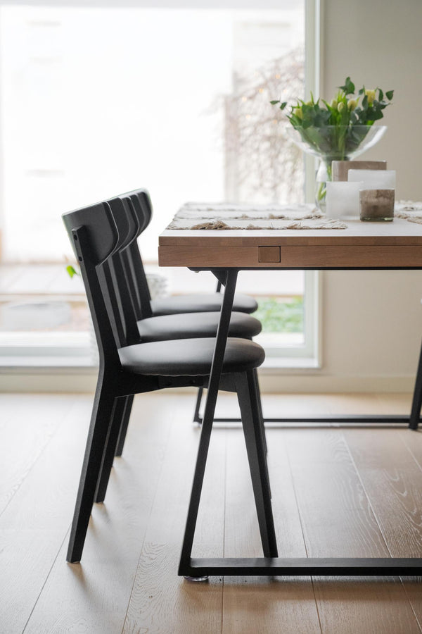 Svart stol med grå dyna vid matbord i trä med blomvas och ljus inredning