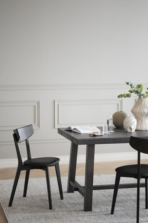 Svart matbord i ek med matchande stolar i minimalistisk matsal med vita väggar och dekorativa vaser