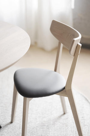 Skandinavisk matstol i ljust trä med vit stoppad sits och elegant ryggstöd vid runt matbord