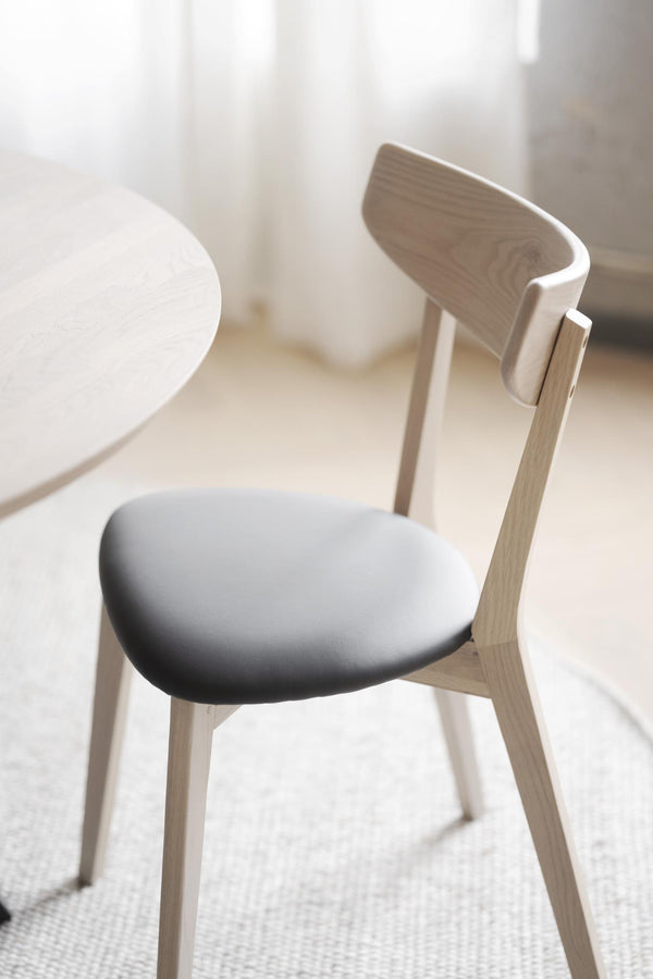 Skandinavisk matstol i ljust trä med vit stoppad sits och elegant ryggstöd vid runt matbord